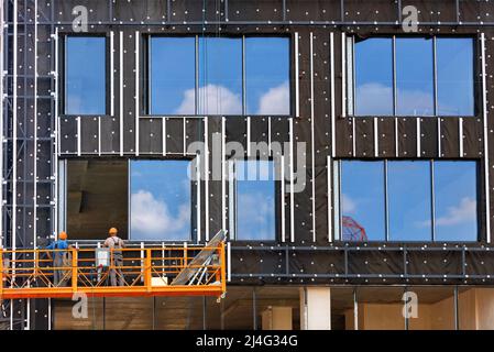 Isolierung der Wände eines Gebäudes im Bau und Installation von großen Fenstern an der Fassade in einem Wohngebäude mit einer Winde und einem Stockfoto