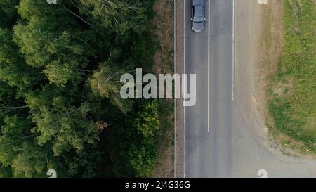 Blick von einem Hubschrauber . Szene . Eine schmale Straße, auf der ein Lastenwagen mit blauer Front und ein Auto mit Anhänger für den Transport unterwegs sind Stockfoto