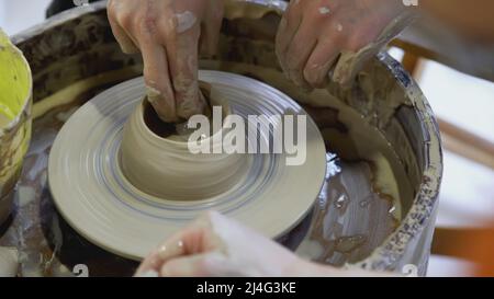 Die Hände eines Kindes auf dem Töpferrad Formen einen Topf. KUNST. Die Hände eines Erwachsenen und eines Kindes in Nahaufnahme sind beim Festival mit Töpferwaren beschäftigt Stockfoto