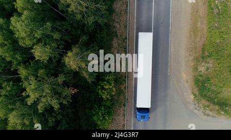 Blick von einem Hubschrauber . Szene . Eine schmale Straße, auf der ein Lastenwagen mit blauer Front und ein Auto mit Anhänger für den Transport unterwegs sind Stockfoto