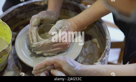 Die Hände eines Kindes auf dem Töpferrad Formen einen Topf. KUNST. Die Hände eines Erwachsenen und eines Kindes in Nahaufnahme sind beim Festival mit Töpferwaren beschäftigt Stockfoto