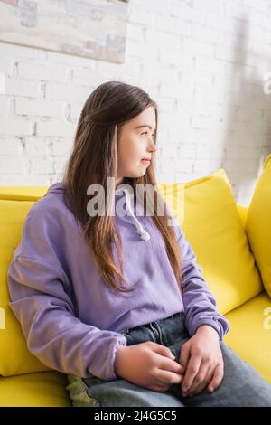 Seitenansicht eines Teenagers mit Down-Syndrom, das zu Hause auf der Couch sitzt Stockfoto