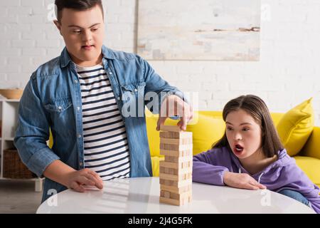 Junge mit Down-Syndrom spielen Holzklötze Spiel in der Nähe geschockt Freund zu Hause Stockfoto