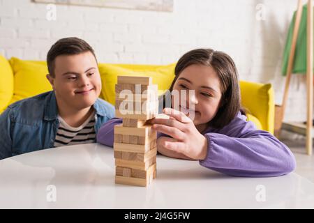 Lächelndes Teenager-Mädchen mit Down-Syndrom spielen Holzblöcke Spiel in der Nähe Freund zu Hause Stockfoto