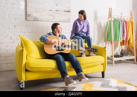 Teenager, der akustische Gitarre spielt und einen Freund mit Down-Syndrom zu Hause ansieht Stockfoto