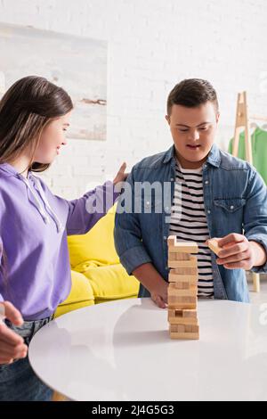 Lächelndes Mädchen mit Down-Syndrom Blick auf Freund spielen Holzklötze Spiel zu Hause Stockfoto