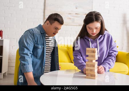 Teen Mädchen mit Down-Syndrom spielen Holzblöcke Spiel in der Nähe Freund im Wohnzimmer Stockfoto