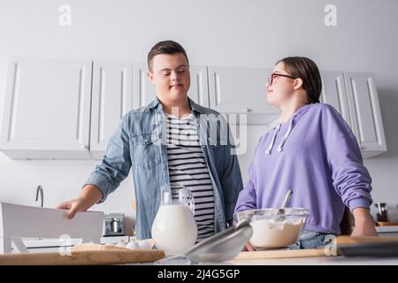 Low-Angle-Ansicht eines Paares mit Down-Syndrom, das in der Nähe von Zutaten in der Küche steht Stockfoto