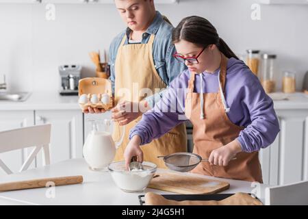 Mädchen mit Down-Syndrom Kochen in der Nähe Freund hält Eier in der Küche Stockfoto