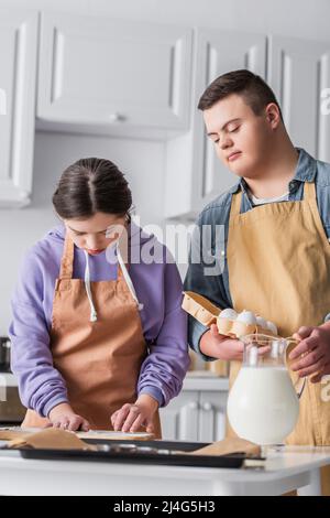 Mädchen mit Down-Syndrom Kochen in der Nähe Freund mit Eiern und Backblech in der Küche Stockfoto