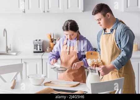 Jugendliche mit Down-Syndrom kochen in der Nähe von Milch und Mehl in der Küche Stockfoto