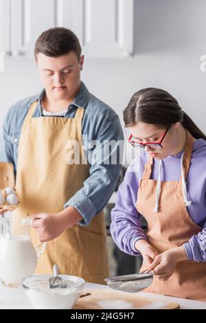 Teenager mit Down-Syndrom Kochen in der Nähe von Mehl und verschwommen Freund in der Küche Stockfoto
