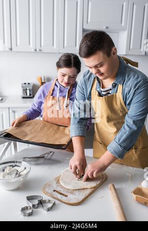 Teenager mit Down-Syndrom macht Cookie in der Nähe Freund mit Backblech in der Küche Stockfoto