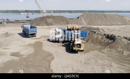 Der Bagger belädt den Muldenkipper mit Sand und Erde. Szene. Luftaufnahme der Ausrüstung bereitet die Baustelle für den Bau eines Stockfoto