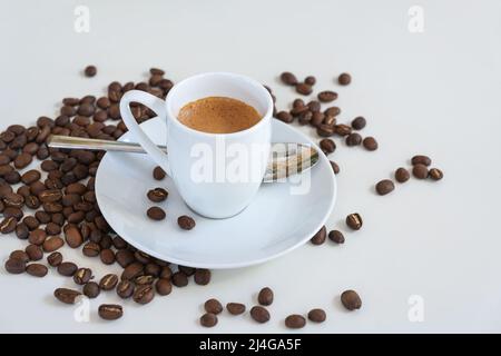 Espresso in einer kleinen Kaffeetasse, Löffel und geröstete Bohnen auf einem weißen Tisch, Kopierraum, ausgewählter Fokus, enge Schärfentiefe Stockfoto