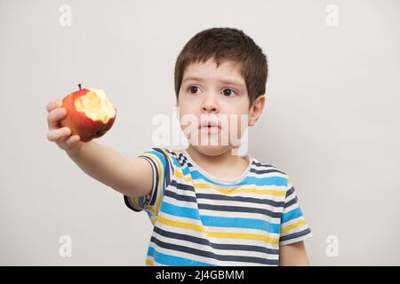 Ein 4-jähriger Junge isst einen roten Apfel und spritzt. Das Kind mag keine Früchte Stockfoto