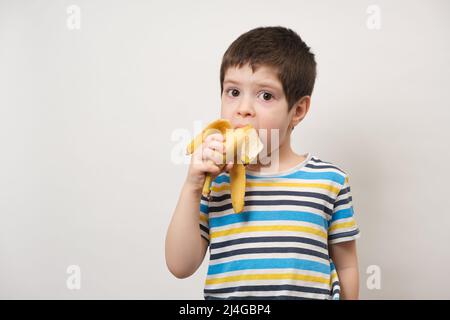 Ein 4-jähriger Junge isst eine Banane. Früchte und Vitamine für Kinder im Vorschulalter Stockfoto