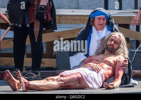 Trafalgar Square, London, Großbritannien. 15. April 2022. ‘Karfreitag an Ostern präsentierte die Besetzung von Wintershall die ‘Passion Jesu’, ein Stück, das die biblische Geschichte Christi durch die „Wunder“, das letzte Abendmahl, Und die Kreuzigung durch die Römer, bevor sie wieder auferstehen, und die Auferstehung, die alle den Trafalgar Square als Bühne für die kostenlose öffentliche Veranstaltung nutzen. Christus wird vom Schauspieler James Burke-Dunsmore dargestellt, der die Rolle seit vielen Jahren spielt. Jesus blutige nach der Entfernung vom Kreuz Stockfoto