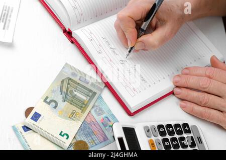 Nahaufnahme der Hände einer älteren Frau, die einen Stift in der Hand hält und an einem Taschenrechner arbeitet. Stockfoto