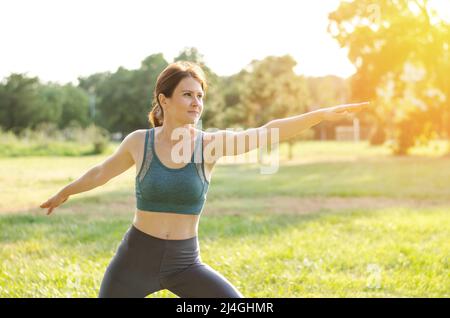 Eine Frau macht Sport in der Natur. Sportliche junge Frau praktiziert Yoga im Park. Sportlerin führt Stretching durch Stockfoto