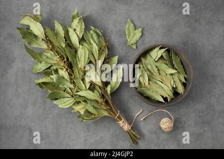 Schüssel mit getrockneten Lorbeerblättern und einem Bund trockener grüner Lorbeerblätter, Draufsicht, flach liegend. Stockfoto