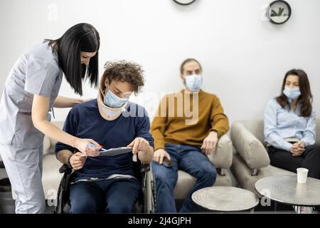 Der Arzt kommuniziert mit dem Rollstuhlfahrer an der Klinikrezeption Stockfoto