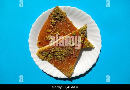 Traditionelles östliches Dessert Kunafa. Draufsicht auf arabischen Käse Kunafa in weißer Platte auf hellblauem Hintergrund. Konafa Stockfoto