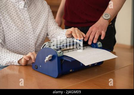 Ein Mann lehrt eine blinde Frau, auf der Braille-Maschine zu tippen. Stockfoto