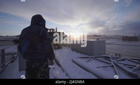 MOSKAU, RUSSLAND - 25. FEBRUAR 2022 : Männer beobachten, wie ein Bulldozer eine schwere Sache wegnimmt. CLIP. Im Norden tragen schwere Geräte Gewichte. Blauer Himmel Stockfoto