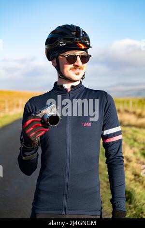 Männlicher Radsportfotograf, der mit seiner Leica M6-Filmkamera in den Yorkshire Dales, Großbritannien, posiert. Stockfoto