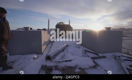 MOSKAU, RUSSLAND - 25. FEBRUAR 2022 : Männer beobachten, wie ein Bulldozer eine schwere Sache wegnimmt. CLIP. Im Norden tragen schwere Geräte Gewichte. Blauer Himmel Stockfoto