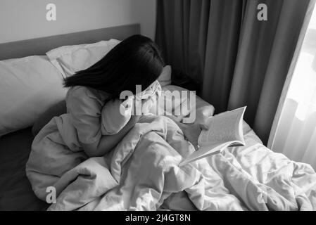 Junge Frau, die auf ihrem gemütlichen Bett sitzt und Notizen zu ihrem Tagebuch macht. Herbststimmung. Streifen Sie Licht und Schatten. Grauton, Schwarz-Weiß-Ton. Stockfoto