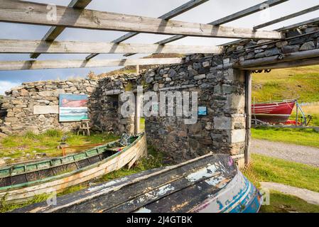 Ein altes, ruiniertes und dachloses Gebäude mit alten Booten bildet eine ungewöhnliche Kunstgalerie in der Skerray Bay an der Nordküste Schottlands direkt vor der NC500. Stockfoto