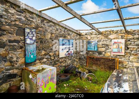 Ein altes, ruiniertes und dachloses Gebäude mit alten Booten bildet eine ungewöhnliche Kunstgalerie in der Skerray Bay an der Nordküste Schottlands direkt vor der NC500. Stockfoto