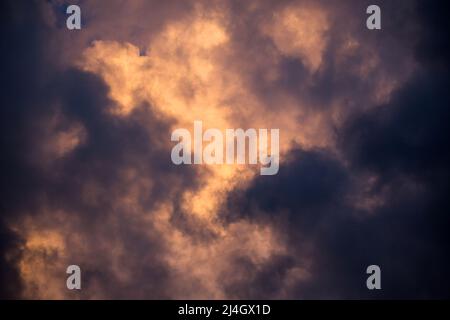 Aufziehende Sturmwolken werden in einem goldenen Ton von der untergehenden Sonne beleuchtet. Stockfoto