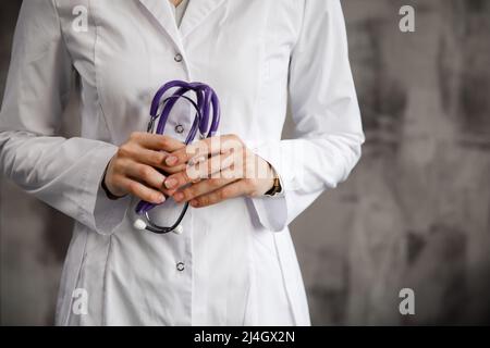 Nahaufnahme einer Ärztin mit einem Stethoskop in den Händen. Vor dem Hintergrund eines verschwommenen Krankenhauses. Stockfoto