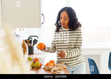 Afroamerikanische Frau in der Küche, die Äpfel und Orangen aussortiert, nachdem sie im Supermarkt einkaufen war Stockfoto