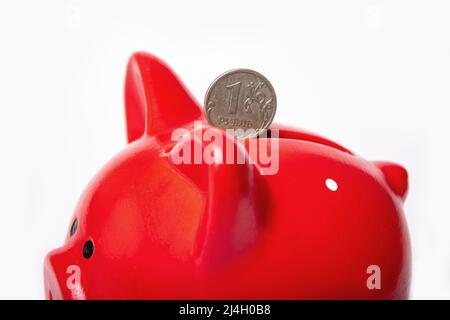 Russische Münze 1 Rubel in einem Loch in einem roten Sparschwein auf weißem Grund. Einsparungskonzept. Die Stabilität der nationalen Währung. Wohlstandskonzept. Stockfoto