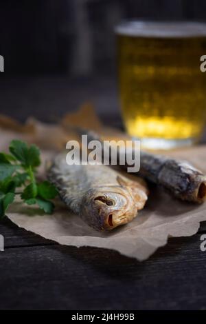 Getrockneter Fisch aus der Nähe, ein Glas Bier aus dem Vintage-Stil auf dunklem Holzboden. Draufsicht. Stockfoto