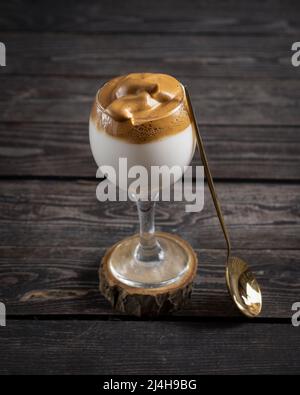 Iced Dalgona Coffee, ein trendiger, flauschiger, cremiger Kaffee auf dunklem Holzhintergrund mit goldenem Löffel Stockfoto