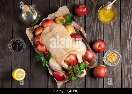 Rohe organische ungekochte junge ganze Ente auf zerknittertem Papier mit Salz und rohen Äpfeln auf schwarzem Textur-Hintergrund. Mit marinierenden Ingre Stockfoto