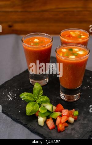 Kleine Gläser Schuss oder Likör mit andalusischem Gazpacho. Eine kalte Gemüse- und Bio-Suppe oder ein Getränk, das im Sommer oder an heißen Tagen getrunken wird. Vertikal oder Stockfoto