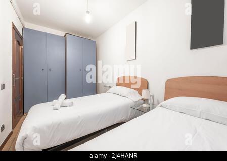 Schlafzimmer mit Twin-Betten mit Kopfteilen aus hellem Holz mit weißen Bettdecken und zwei grauen Schränken Stockfoto