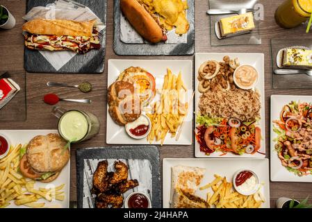 Fastfood-Gerichte mit Basmati-Reis mit Tintenfisch, Hot Dogs, verschiedene Burger, Sandwich mit Sauce und Pommes, Desserts und Kuchen, Grillflügel Stockfoto