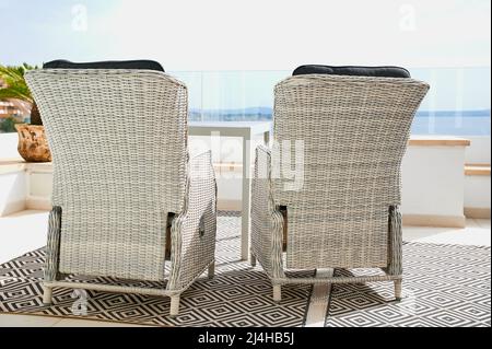 Zwei weiße Rattanstühle auf einem Balkon an einem sonnigen Tag Stockfoto