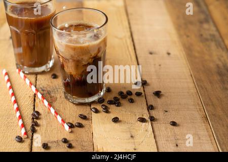 Eiskaffee in großen transparenten Gläsern, über Milch gegossen, mit Kaffeebohnen auf Holzboden, sommerliches kühlendes Getränk, mit Kopierplatz Stockfoto