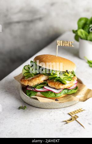 Hausgemachter Burger mit Fleisch, Spinat, Gurke, Rettich und Microgreens. Fastfood auf Teller auf strukturiertem Hintergrund. Nahaufnahme Stockfoto