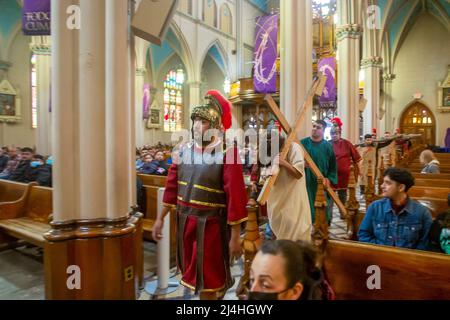 Detroit, Michigan, USA. 15. April 2022. Jesus trägt ein Kreuz und trägt eine Dornenkrone während der Lebendigen Stationen des Kreuzes in der Basilika Ste. Anne de Detroit. Ste. Anne wurde 1701 von französischen Siedlern gegründet. Der Karfreitagsdienst wurde in spanischer Sprache gehalten, was die derzeitige Mitgliedschaft in der Pfarrei widerspiegelt. Kredit: Jim West/Alamy Live Nachrichten Stockfoto