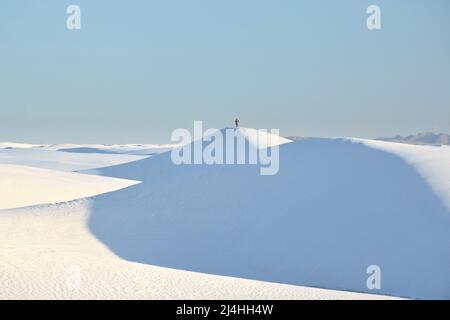 Auf einer riesigen Sanddüne unter einem hellen azurblauen Himmel steht eine einsam-menschliche Figur Stockfoto