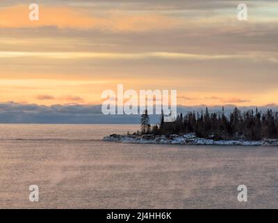 Bei Sonnenaufgang steigt aus dem kalten, von Kiefern gesäumten Wasser des Lake Superior Dampf auf Stockfoto